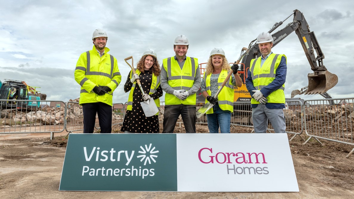 5 people in front of a digger holding spades