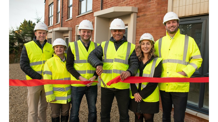 Group of men and women in hard hats and high-vis jackets in front of completed homes. Mayor Marvin Rees is in the centre cutting a red ribbon.